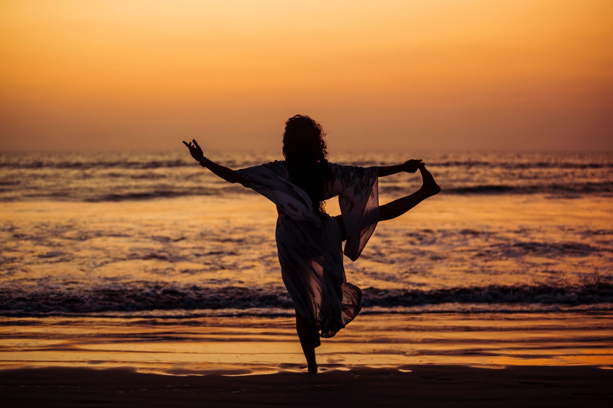 Woman practicing yoga on a beach at sunrise for wellness and restoration